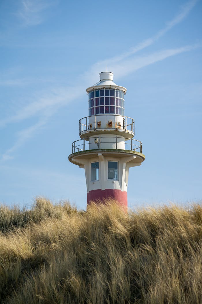 A scenic view of a lighthouse rising above grassy coastal dunes against a clear sky.